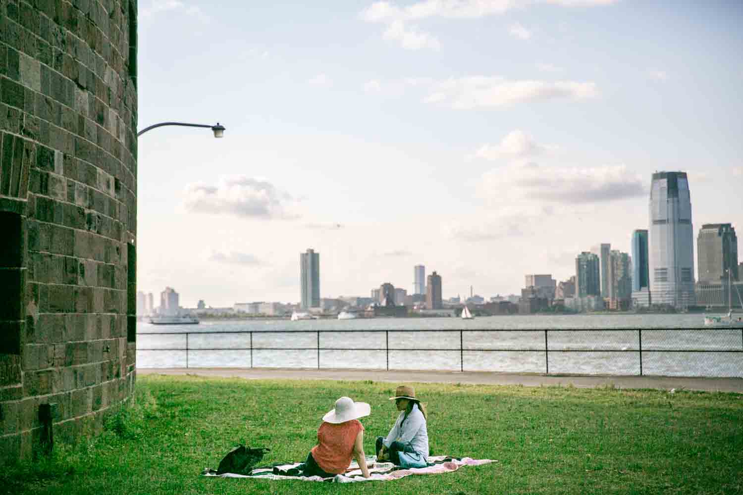 Governors Island photos of two women sitting in grass with NYC skyline in background