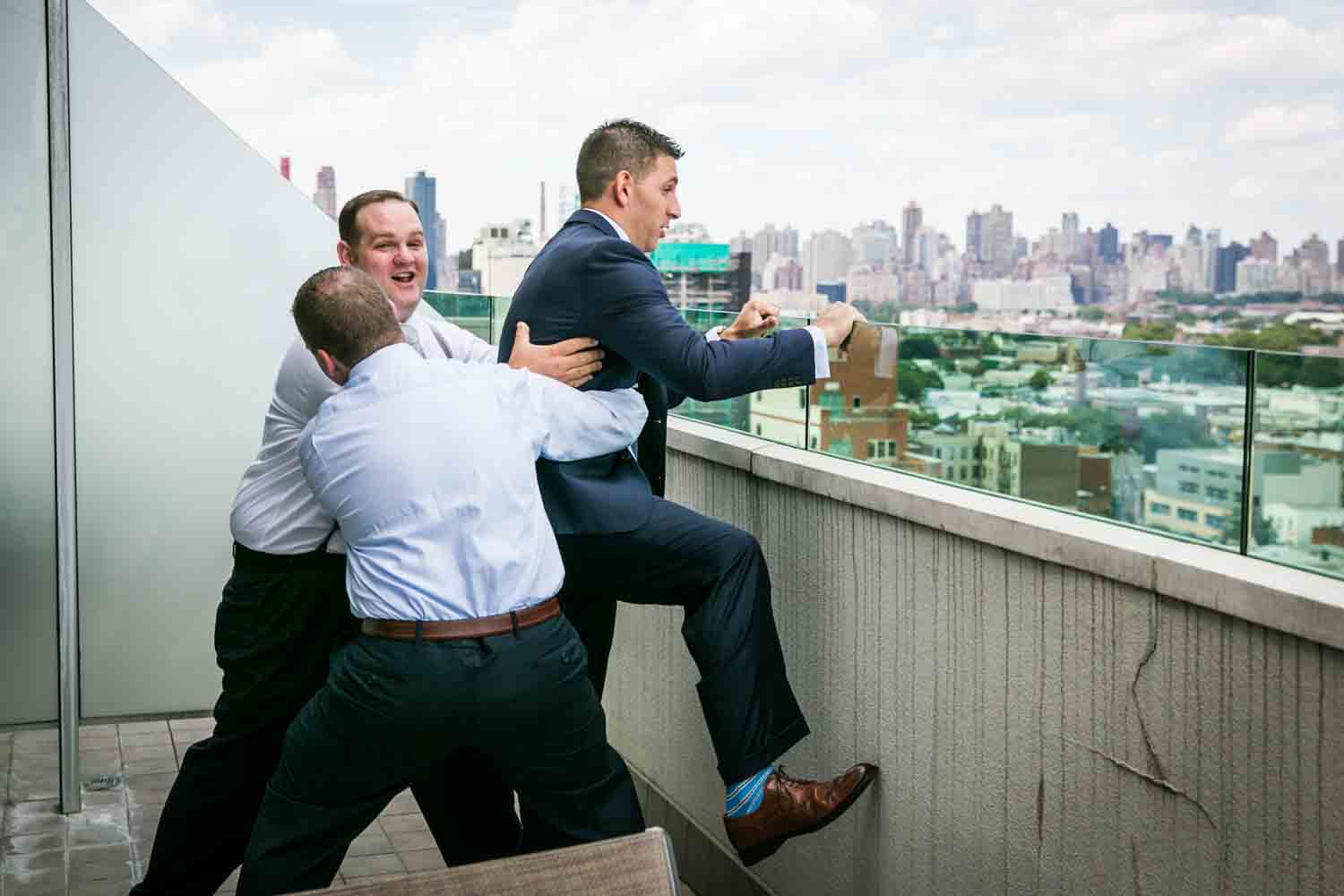 Groom attempting to leap from balcony and held back by two groomsmen