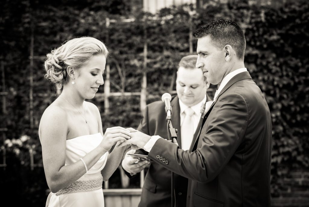 Black and white photo of bride putting ring on groom's finger