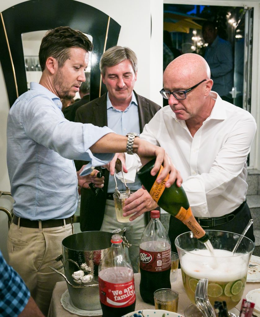 Man pouring champagne into a punch bowl with two guests