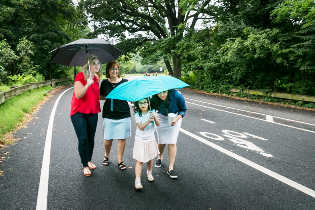 Three woman and little girl walking down road under umbrellas