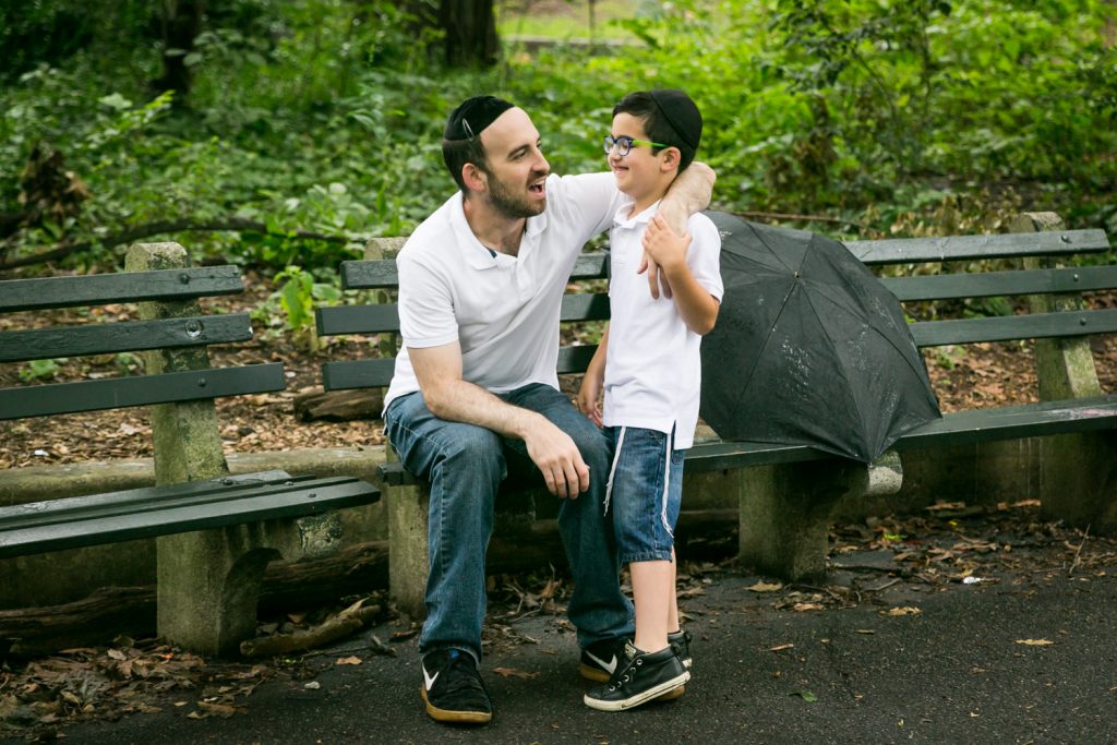 Father sitting on bench in Prospect Park with arm around son