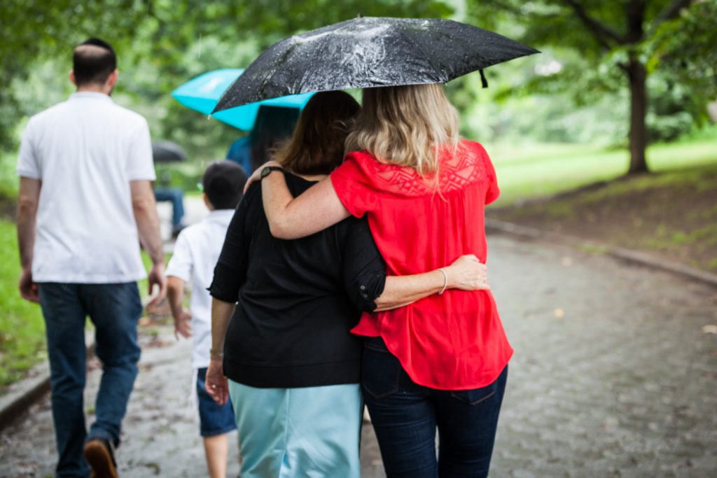 Two women hugging under umbrella and walking away