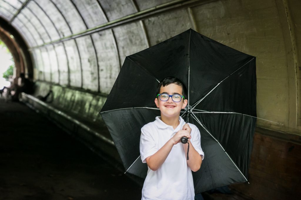 Prospect Park family photos of a little boy wearing glasses and holding a black umbrella