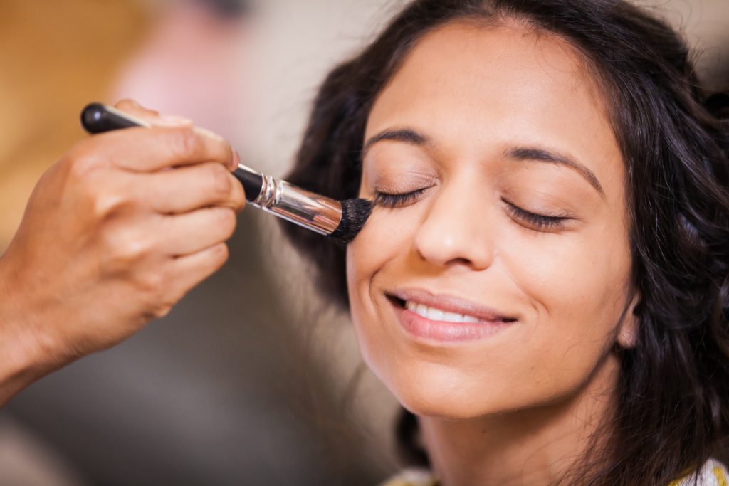 Close up of hand applying makeup to bride's face for an article on when should my wedding photographer arrive