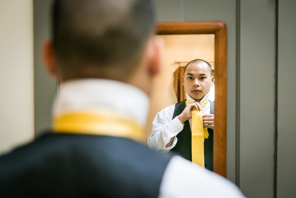 Groom putting on tie in mirror for an article on when should my wedding photographer arrive