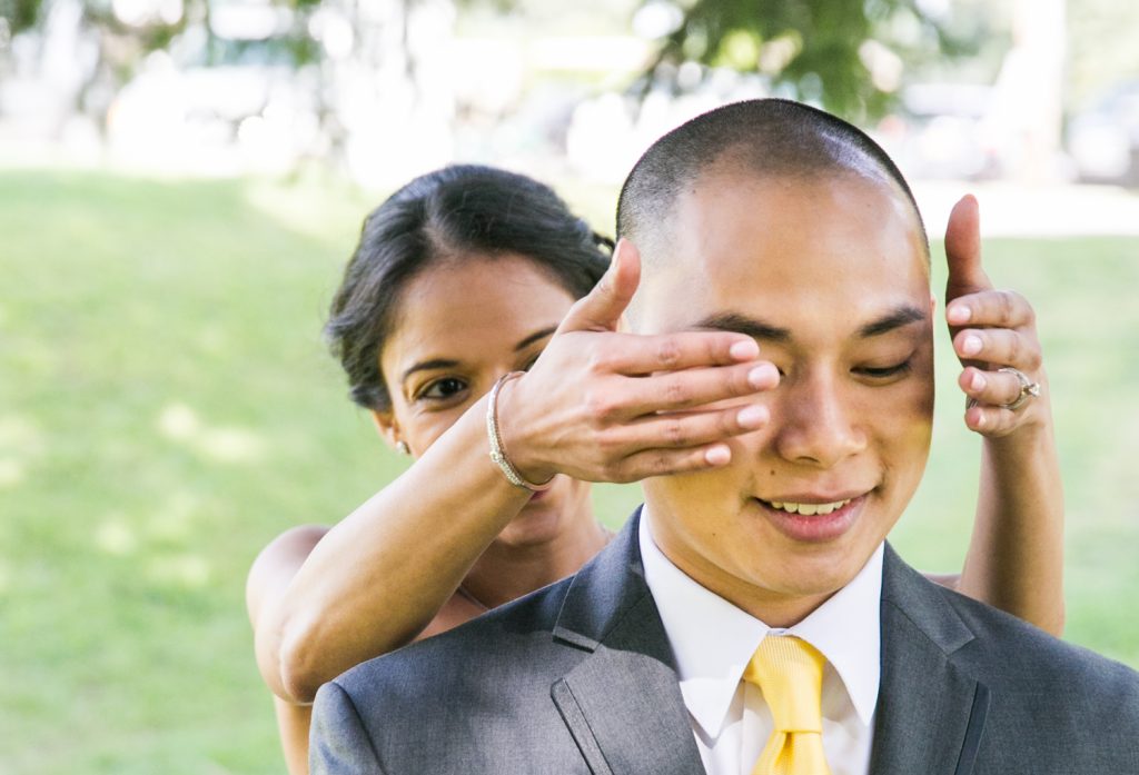 Bride putting hands over groom's eyes for an article on when should my wedding photographer arrive