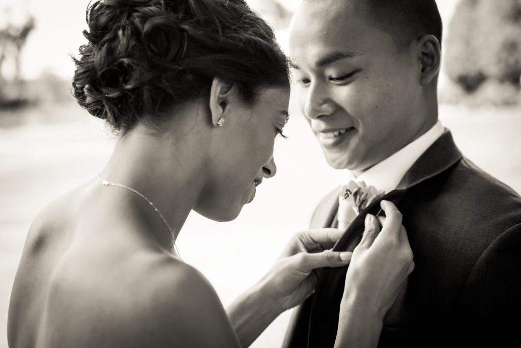 Black and white photo of bride putting boutonniere on groom