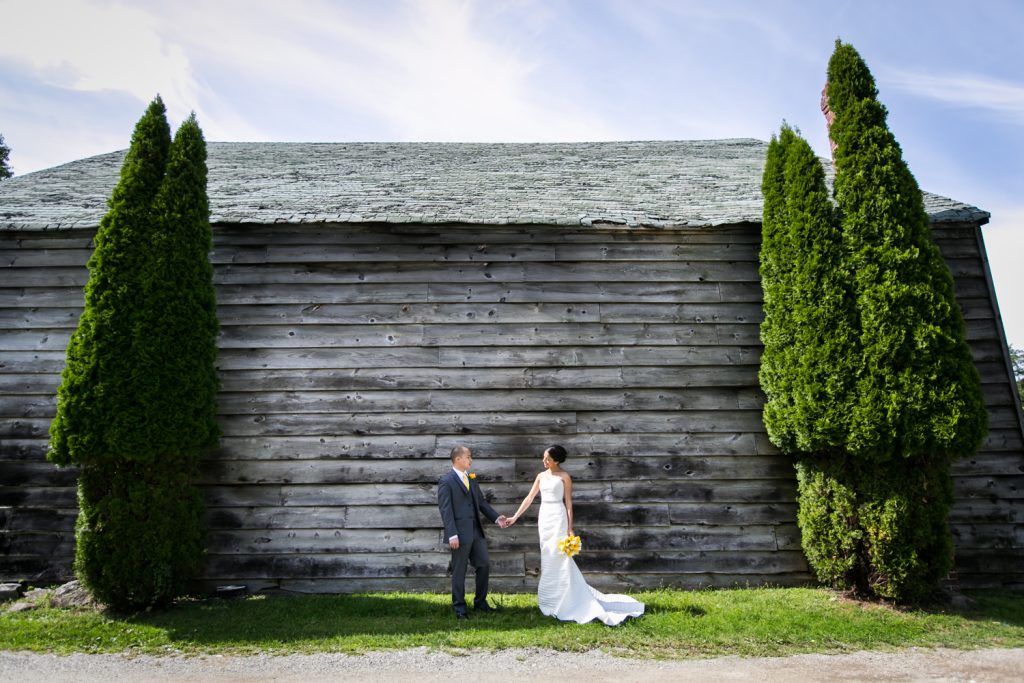 Bride and groom holding hands in front of wooden shed for an article on when should my wedding photographer arrive