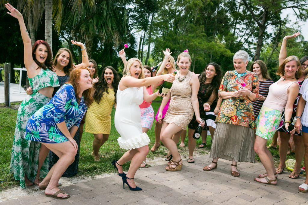 Bride-to-be opening bottle of champagne with cheering guests