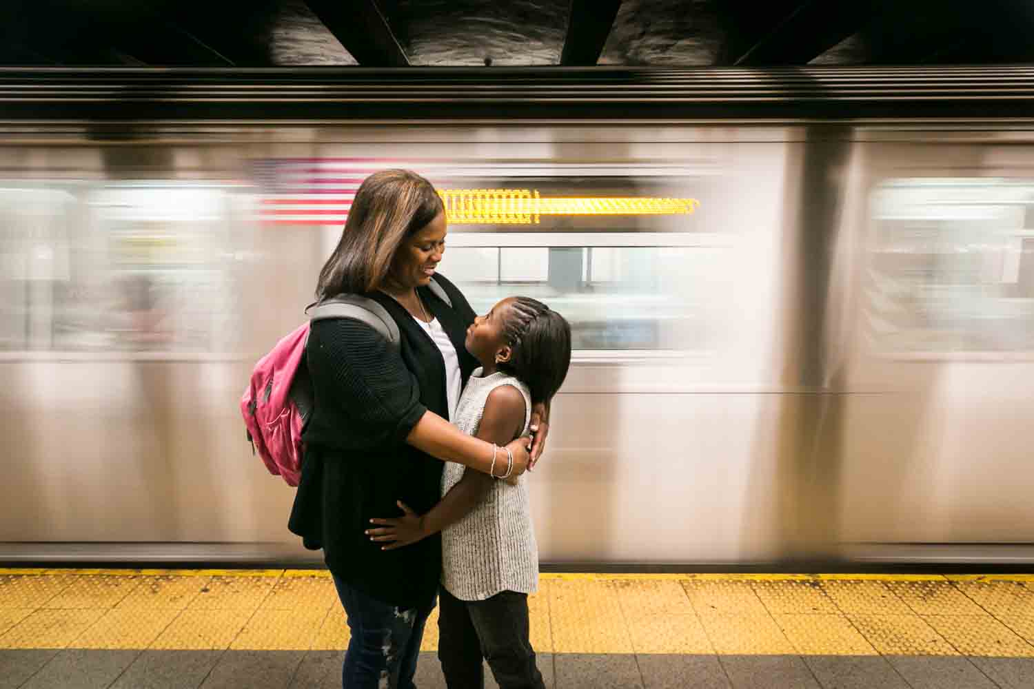 Mother and daughter hugging with speeding subway train in background