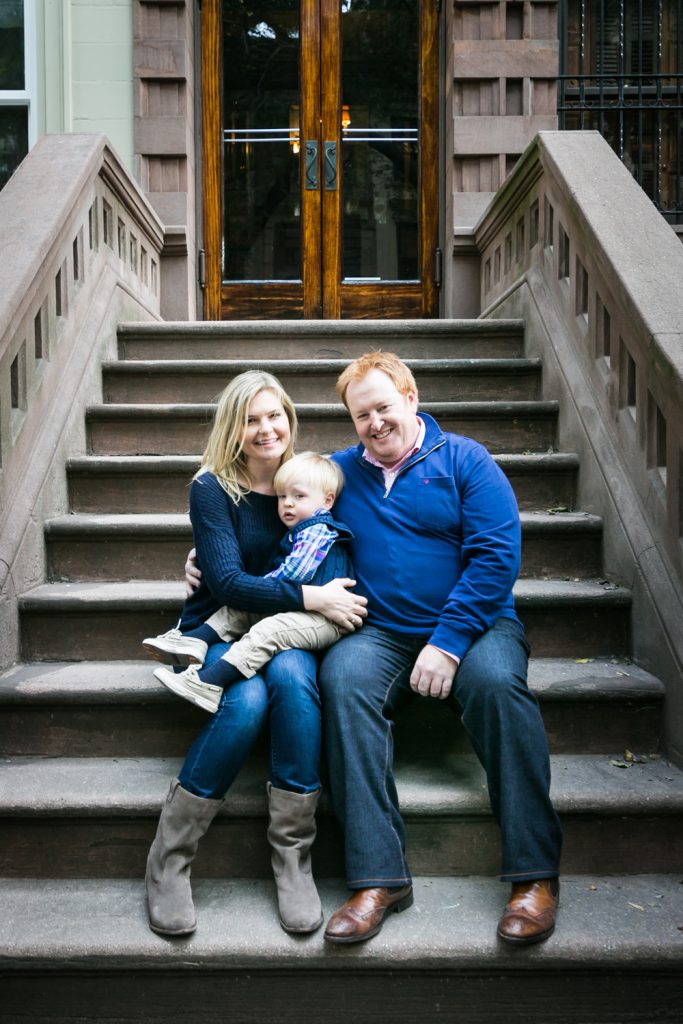 Family portrait of mother, father, and little boy sitting on brownstone steps