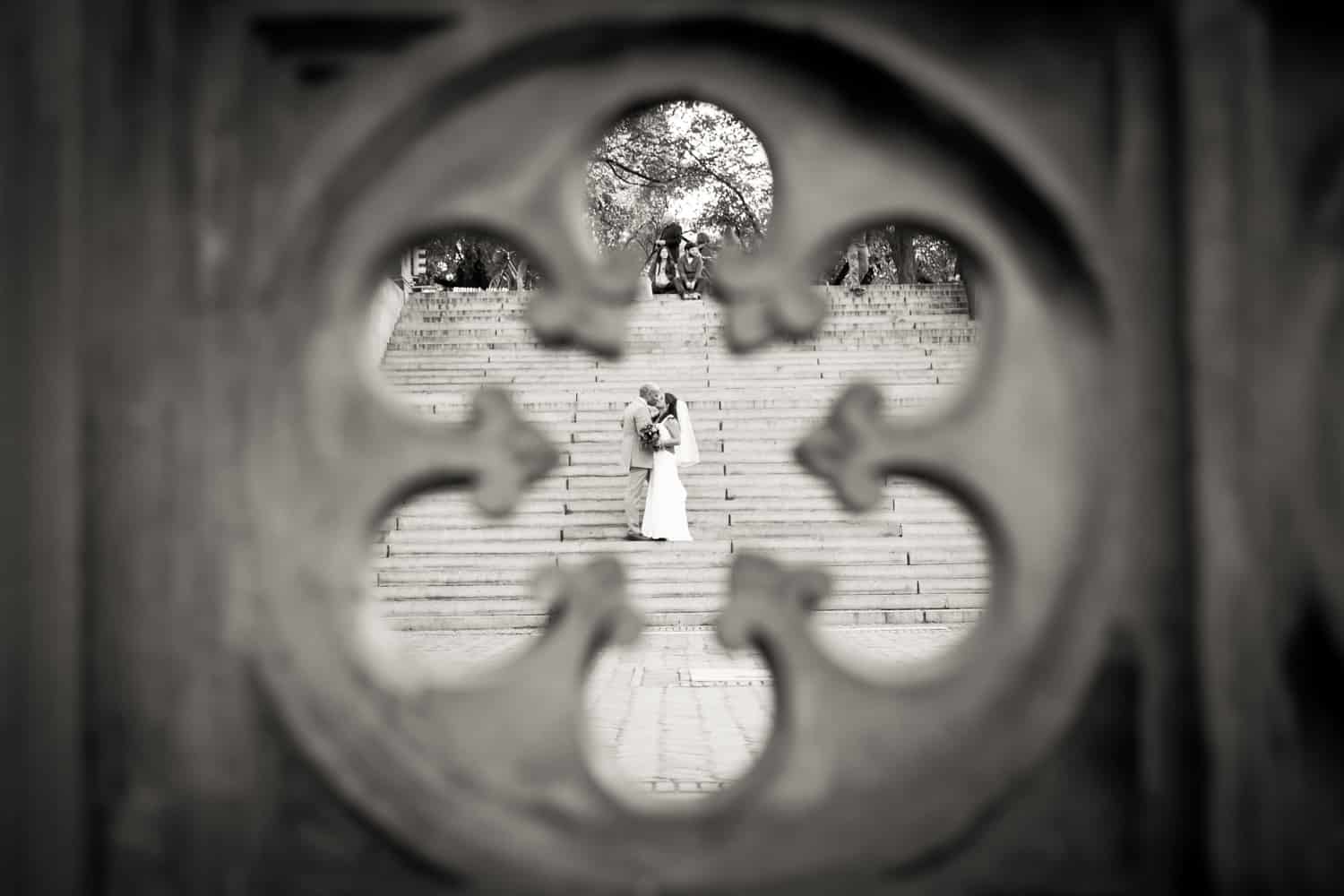 Black and white photo of bride and groom on stairs as views through Central Park fence