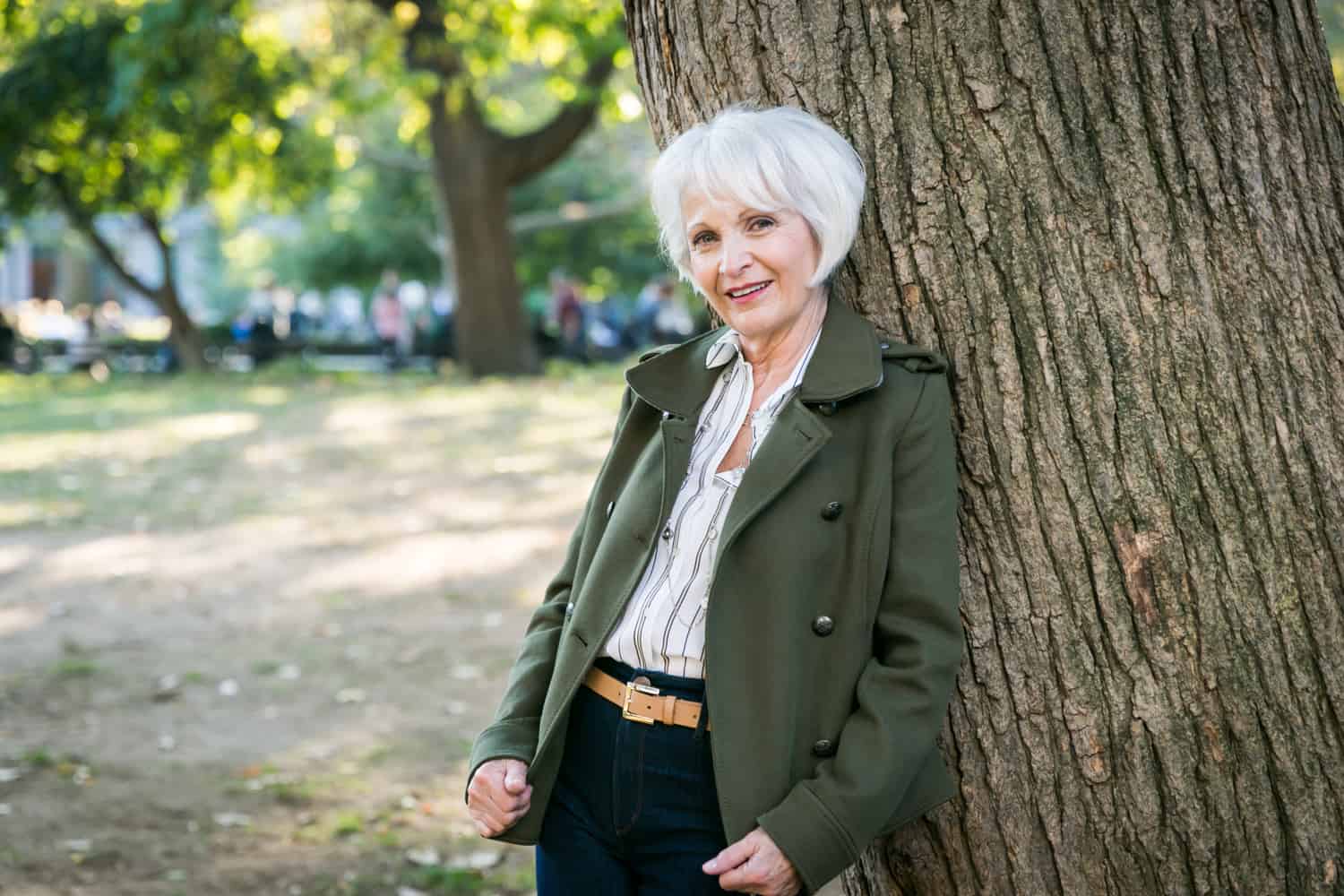 Older woman in olive jacket standing by tree