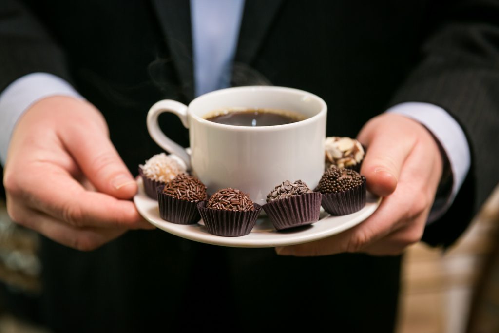 Hands holding a cup of coffee with chocolates around the plate for article on creative guest favors