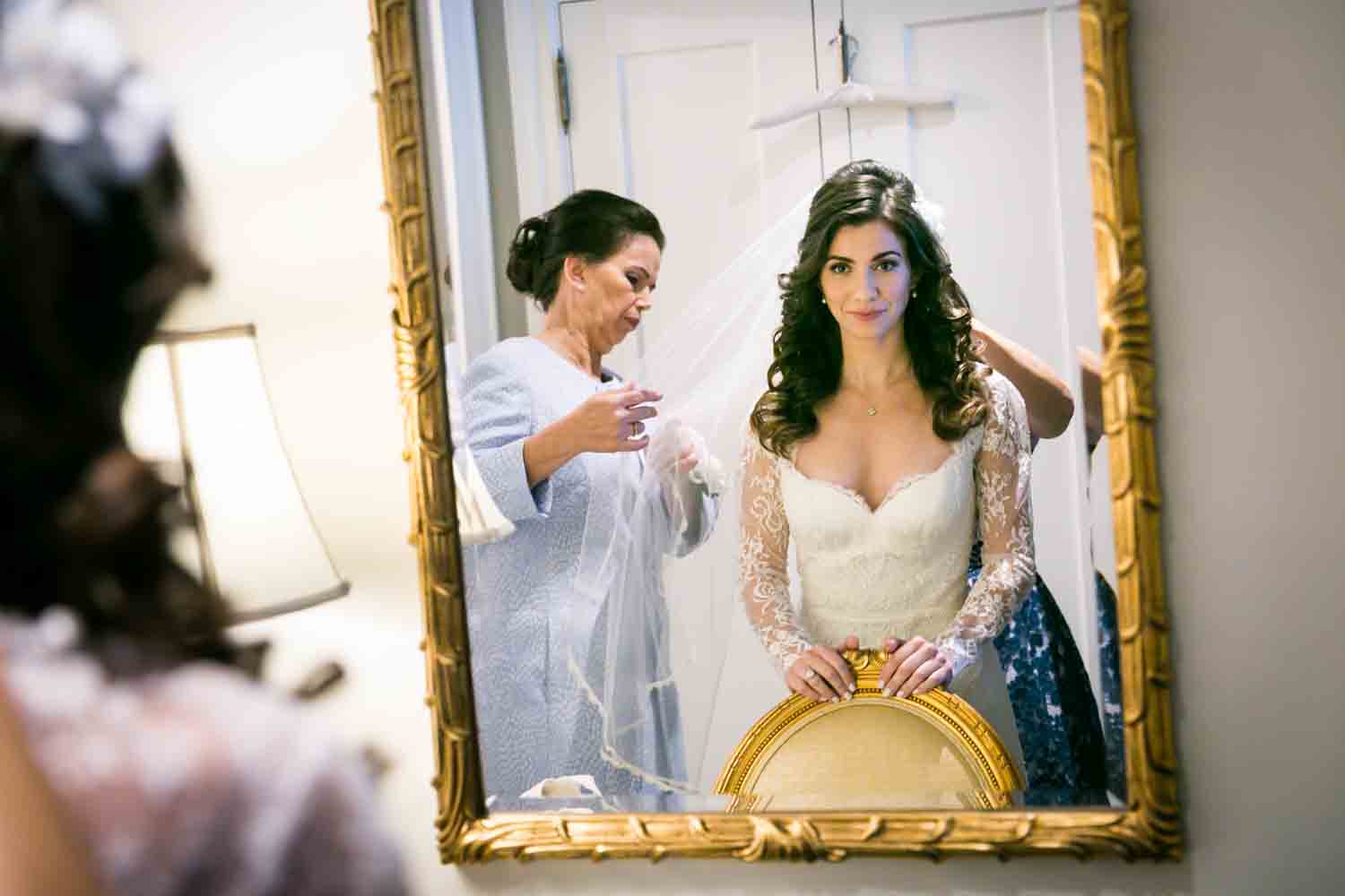 Reflection of bride in mirror putting on veil at a Loeb Boathouse wedding in Central Park