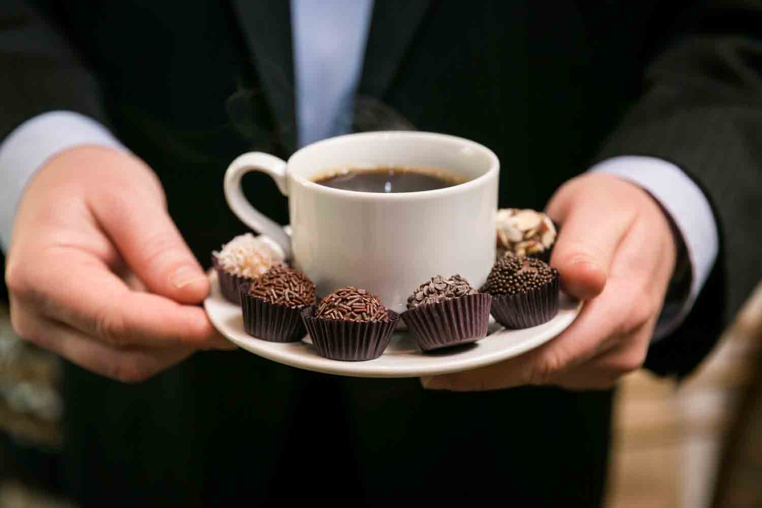 Close up on hands holding coffee cup with brigadeiro candies around the cup