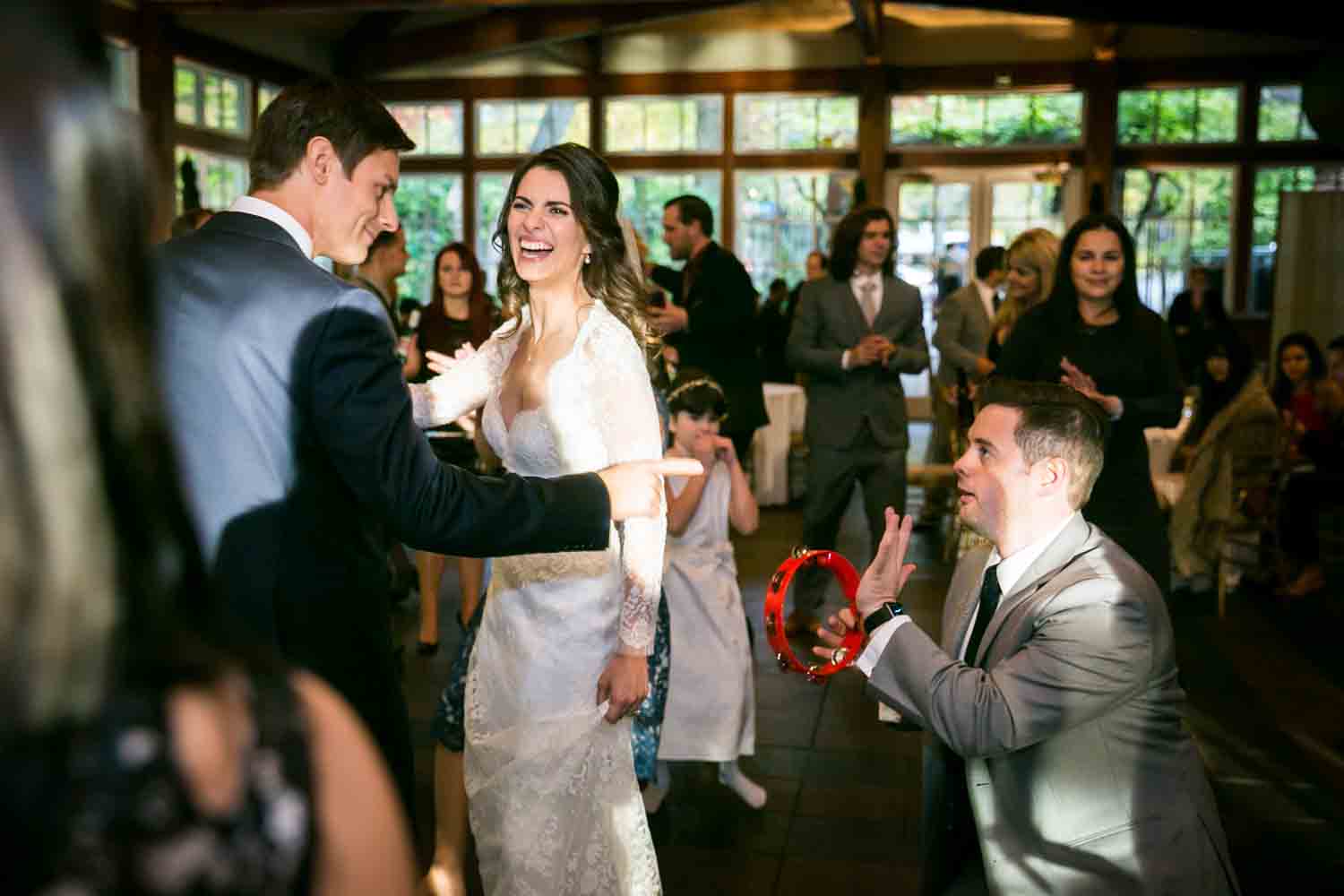 Bride and groom with guest on his knees playing a tambourine