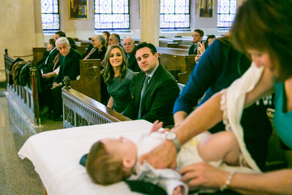 Parents watching baby during ceremony by NYC Greek orthodox baptism photographer, Kelly Williams