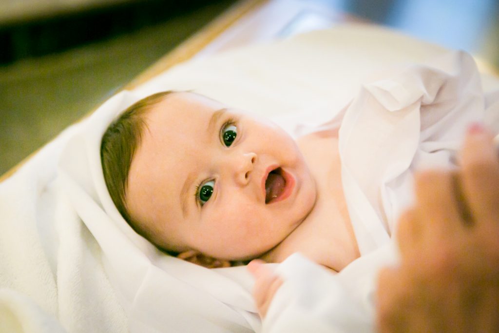 Baby wrapped in towel by NYC Greek orthodox baptism photographer, Kelly Williams