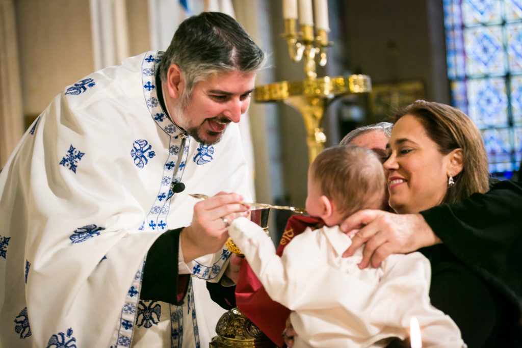 Priest giving spoon to baby by NYC Greek orthodox baptism photographer, Kelly Williams