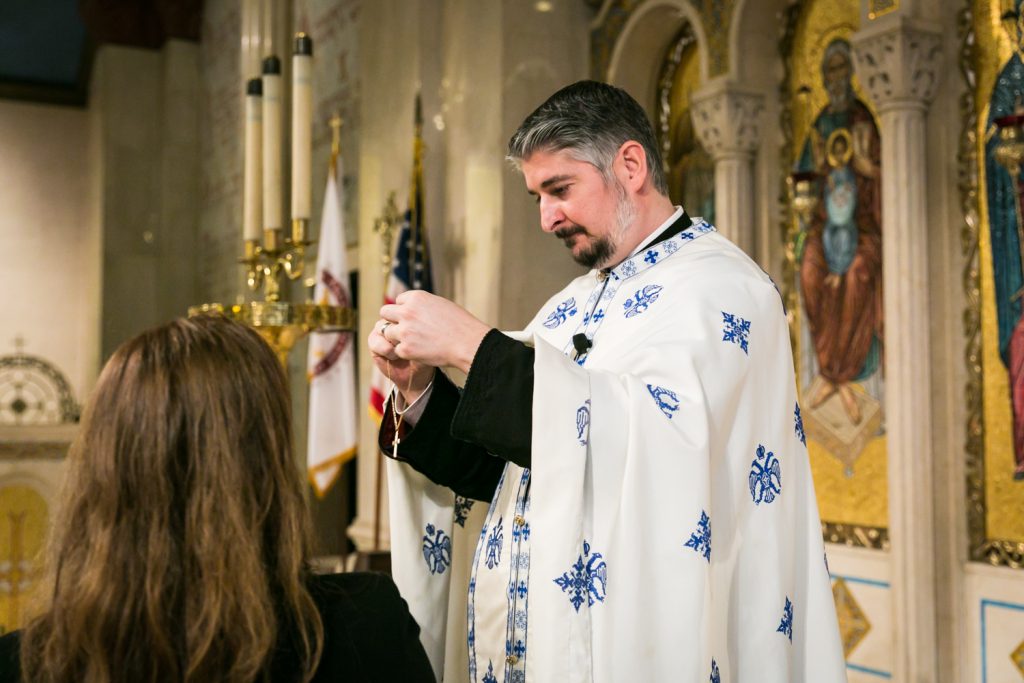 Priest holding necklace with crucifix by NYC Greek orthodox baptism photographer, Kelly Williams