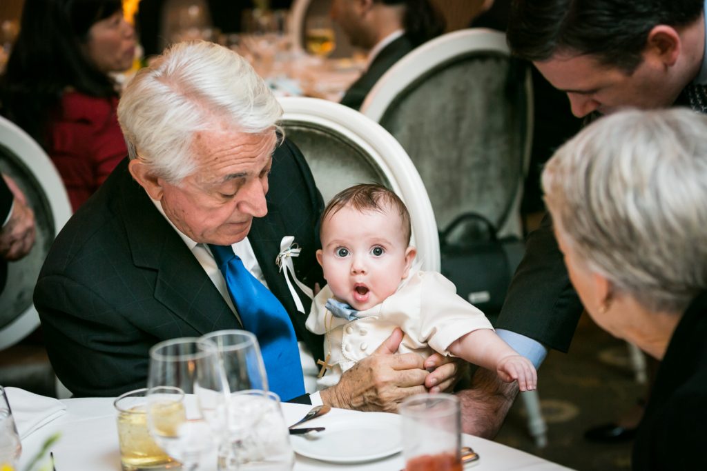 Grandfather holding surprised baby by NYC Greek orthodox baptism photographer, Kelly Williams