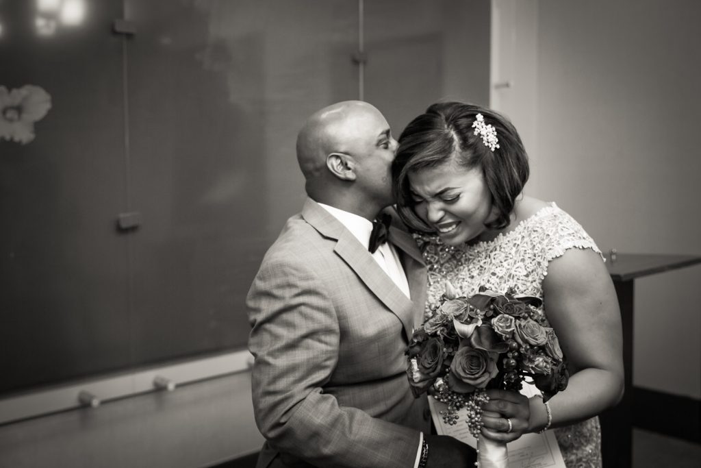 Black and white photo of groom kissing bride on her head