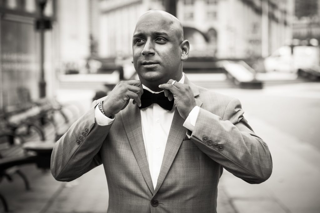 Black and white photo of groom adjusting bow tie for an article on wedding website tips