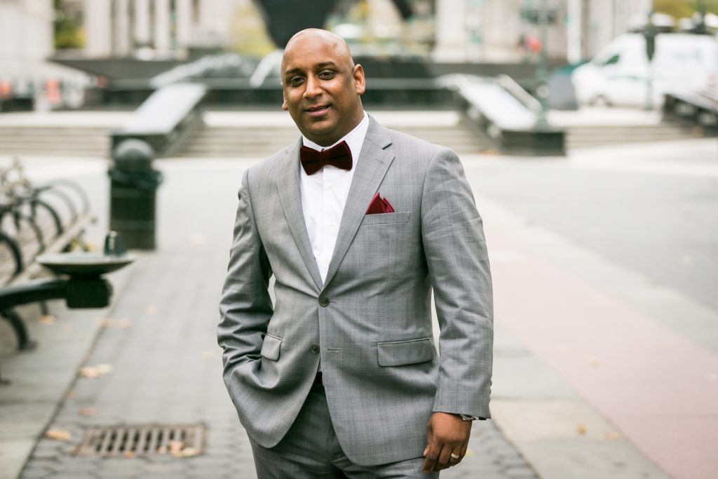 Groom wearing grey coat and red velvet bow tie for an article on wedding website tips