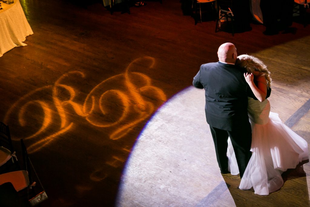 Bride dancing with father with initials in light on dance floor for an article on how DJ lighting affects your wedding photos