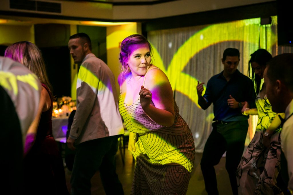 Woman bathed in pink and yellow light dancing at reception for an article on how DJ lighting affects your wedding photos