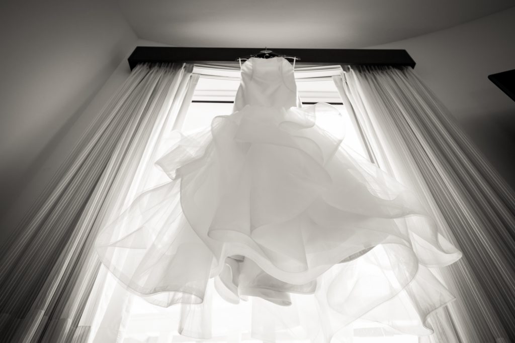 Black and white photo of wedding dress hanging in a window for an article on how to have an unplugged wedding