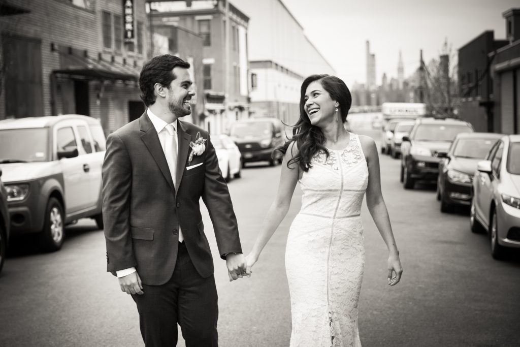 Black and white photo of bride and groom walking hand in hand on Brooklyn street
