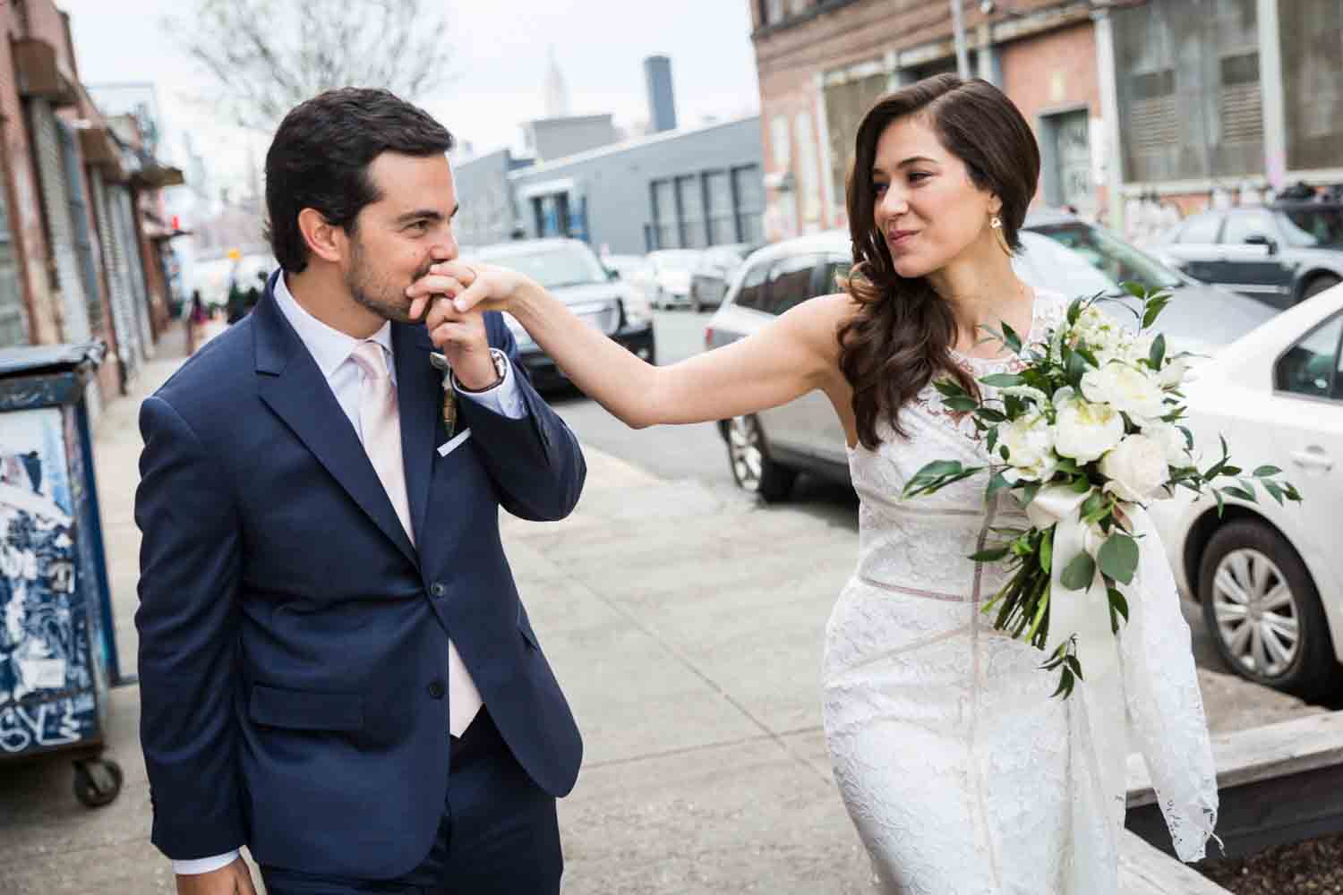 Groom kissing bride's hand on Brooklyn sidewalk