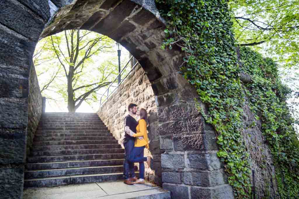 Kissing couple under arch at a Fort Tryon Park engagement portrait