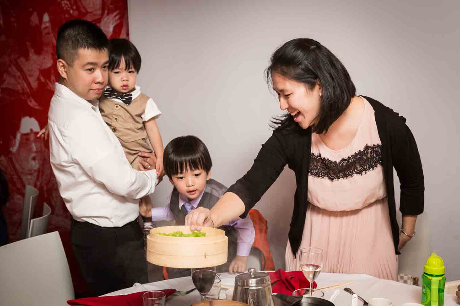 Woman putting bamboo steamer on table in front of family at a Chinatown rehearsal dinner