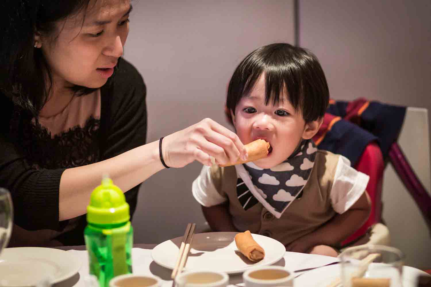 Mother feeding egg roll to little boy at a Chinatown rehearsal dinner