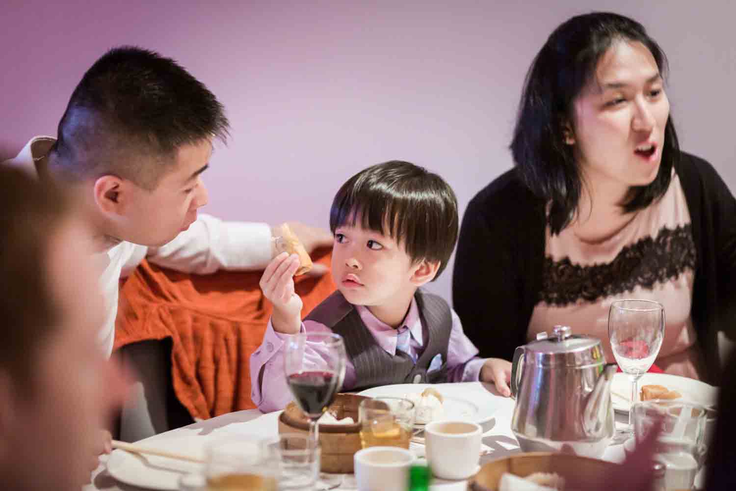 Little boy trying to give food to his father at a Chinatown rehearsal dinner