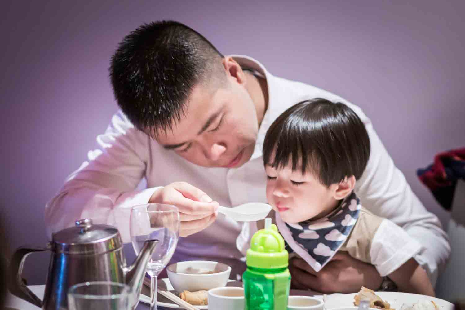 Father feeding soup to little boy at a Chinatown rehearsal dinner
