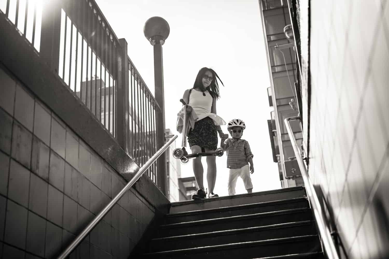 Black and white photo of mother and little boy walking down subway station stairs