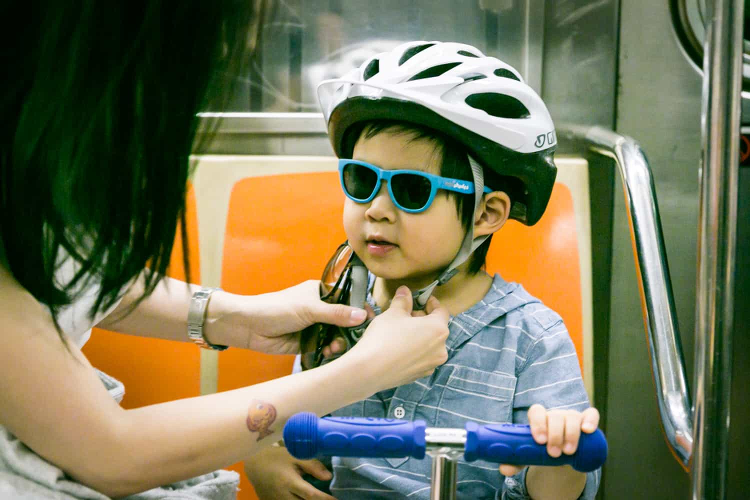 Mother attaching helmet on little boy wearing sunglasses