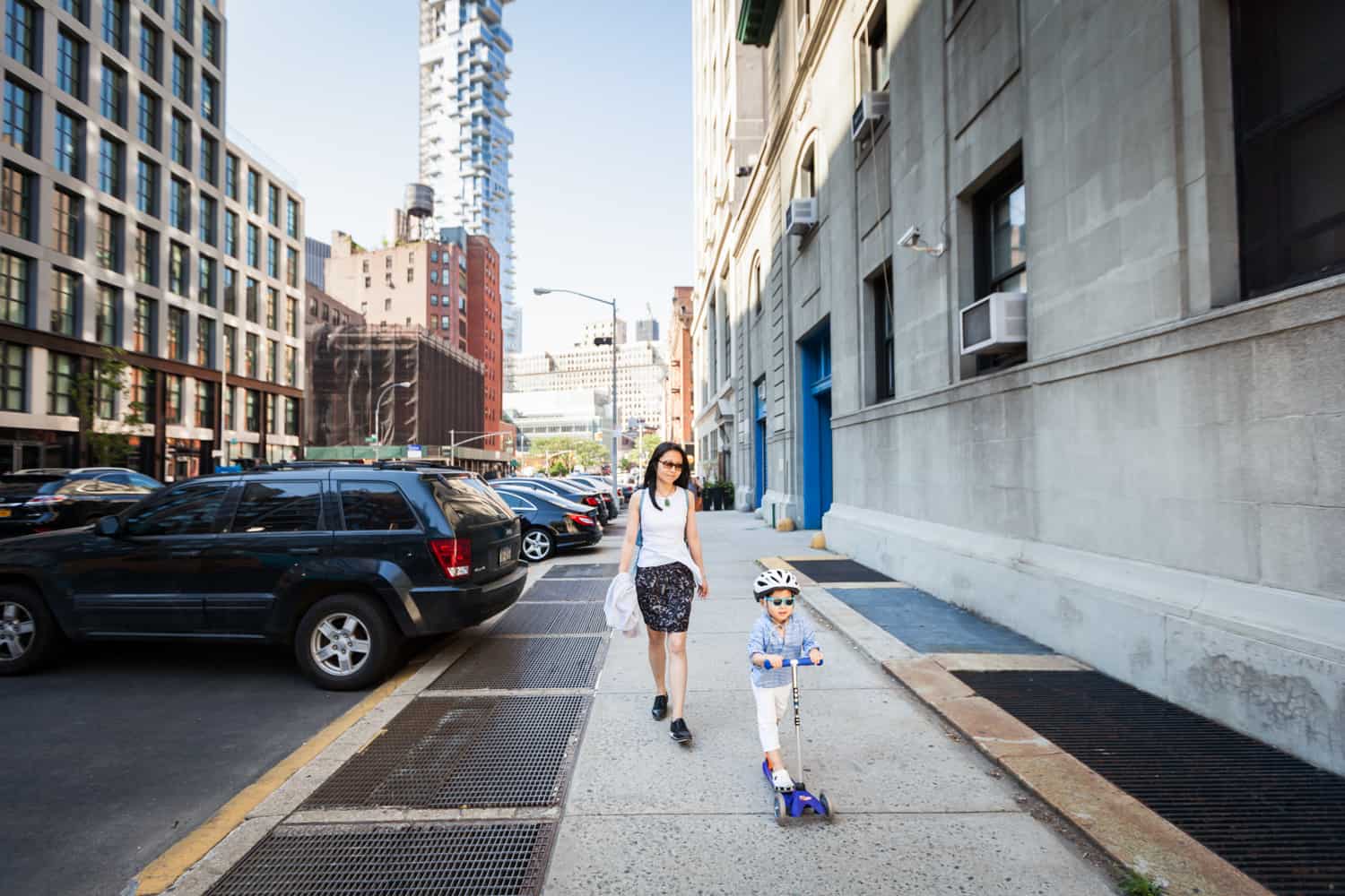 Mother and little boy on scooter walking on NYC sidewalk