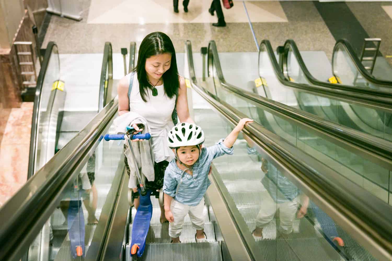 Mother and little boy wearing helmet going up on escalator