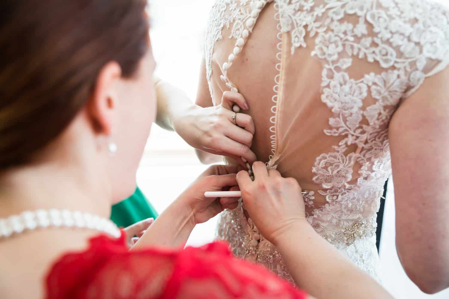 Close up on hands buttoning up bride into wedding dress