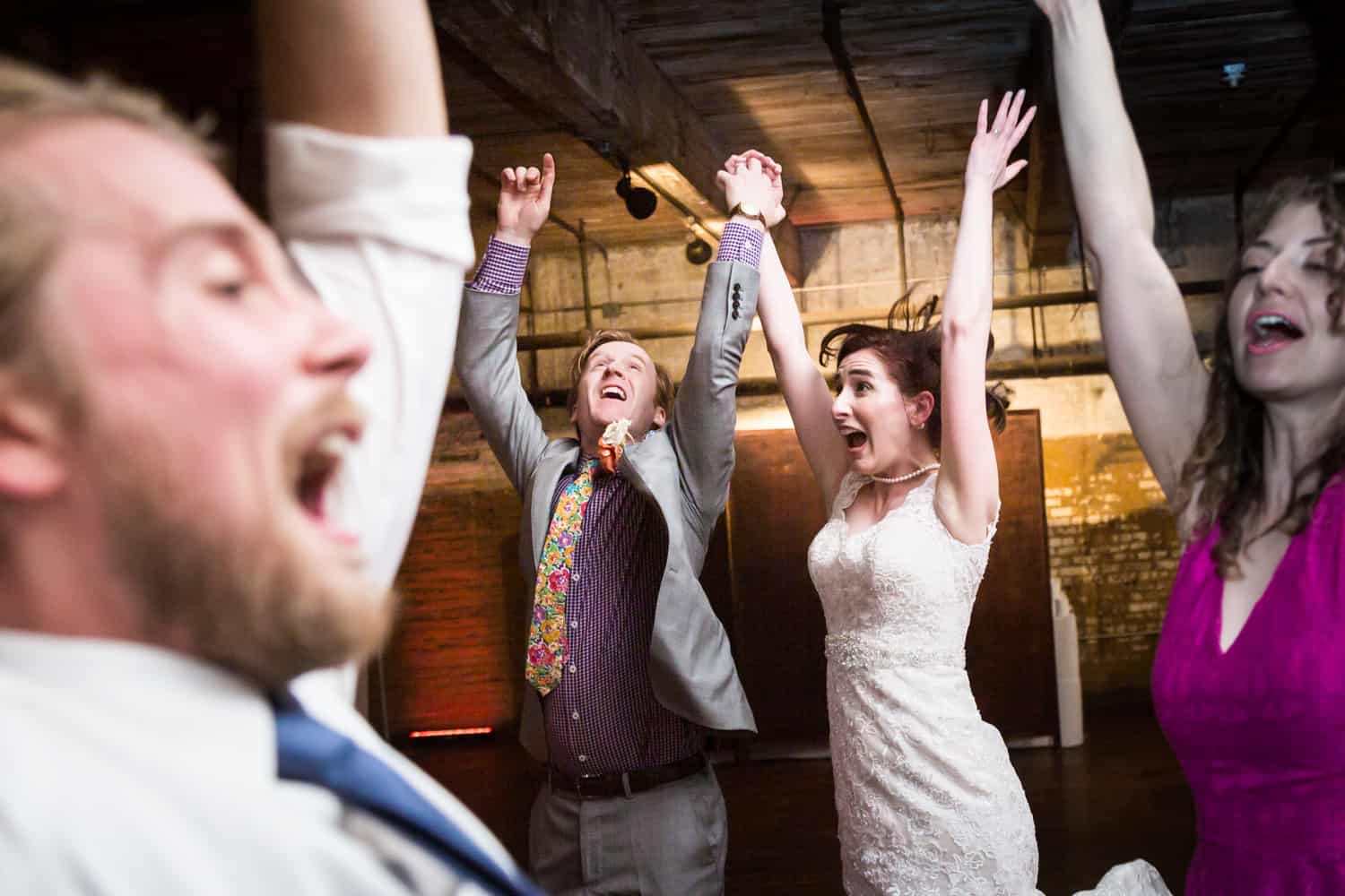 Bride and groom dancing with guests with arms raised at a Greenpoint Loft wedding