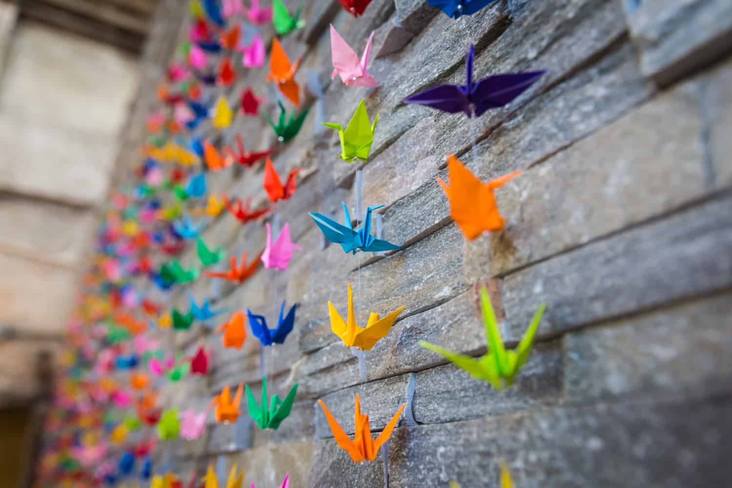 Stone wall with multicolored origami cranes hanging over the wall
