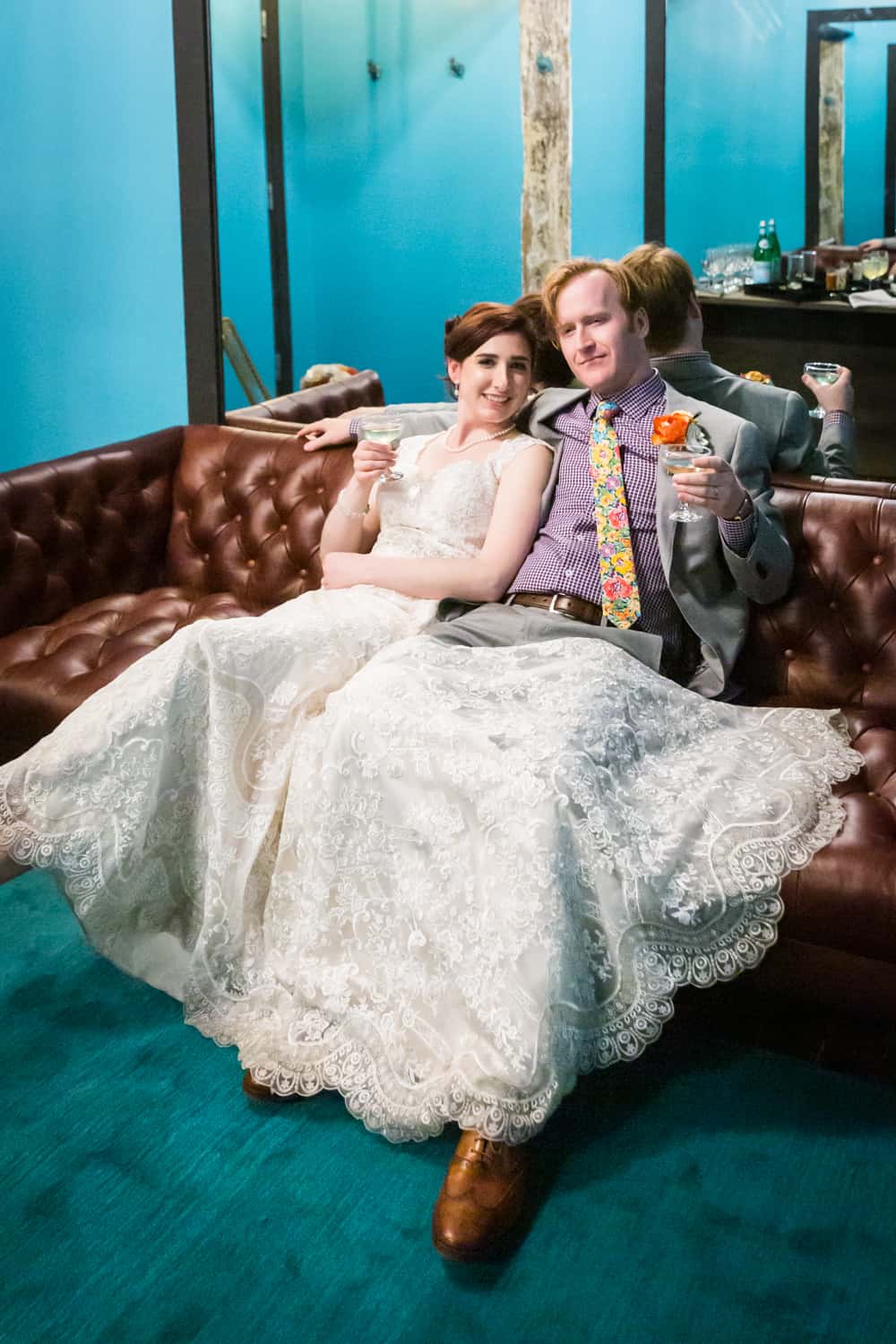 Bride and groom holding cocktails and lounging on couch at a Greenpoint Loft wedding