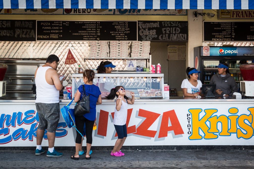 Kid with sunglasses dancing in front of a Coney Island hot dog stand