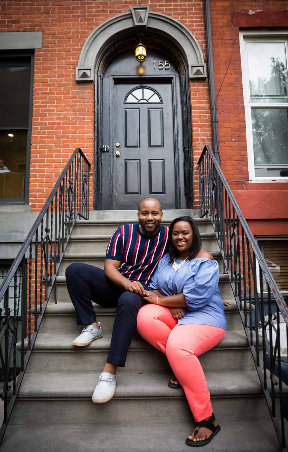 African American couple sitting on stairs in front of Brooklyn brownstone